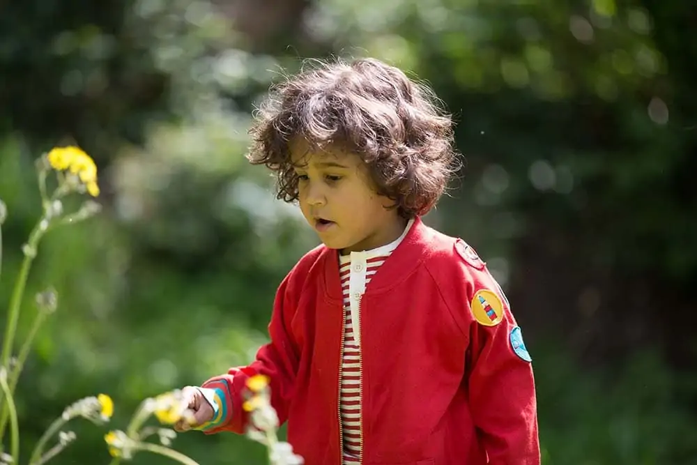 Child modelling Little Green Radicals clothes by some flowers outside