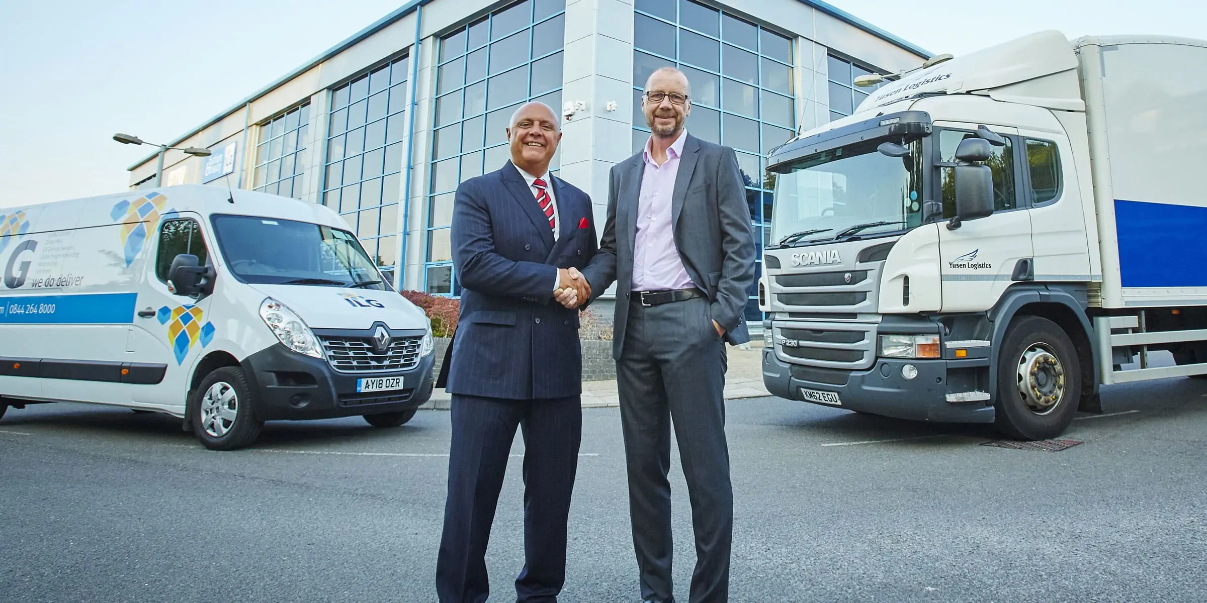 two men standing in front of a warehouse building shaking hands