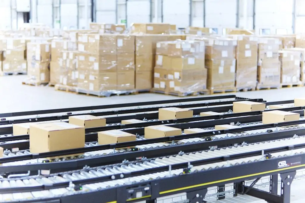 orders on a conveyor belt in the warehouse with stacks of pallets behind it