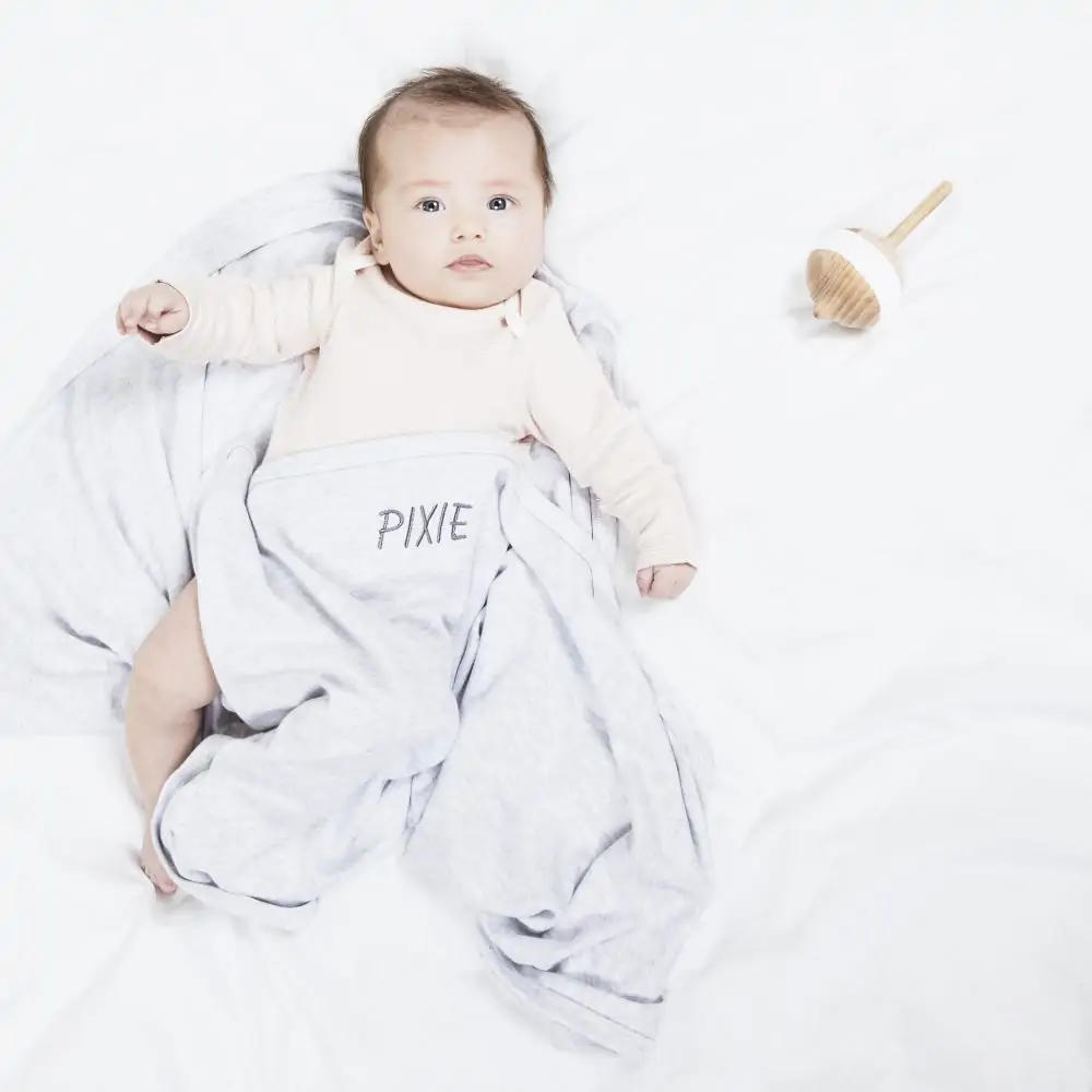 Baby wrapped up in a Mori blanket embroidered with the name Pixie