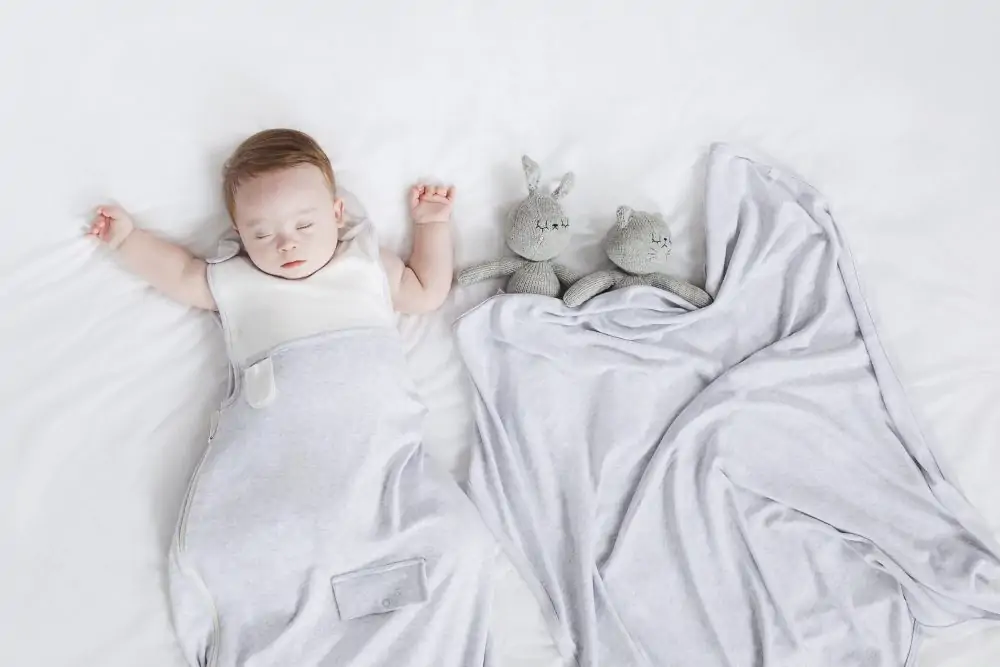 Baby sleeping in a mori sleep suit next to teddy bears