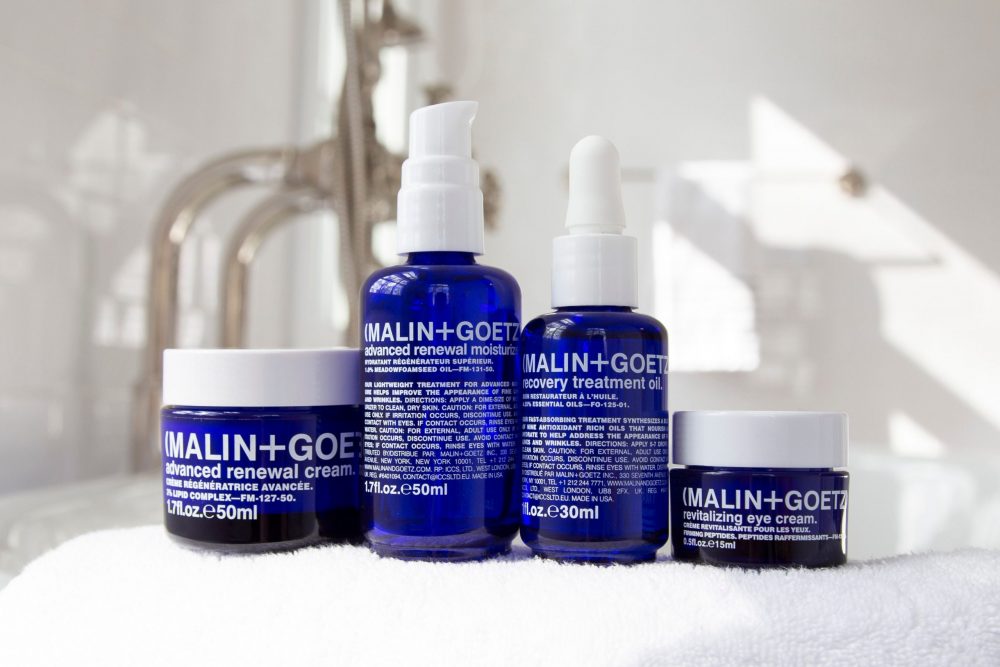Malin + Goetz products lined up on the side of a bath