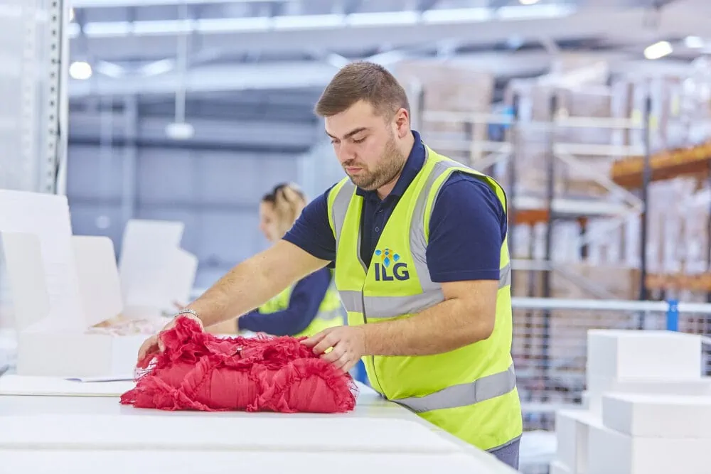Man folds red dress in warehouse ready to pack into a box
