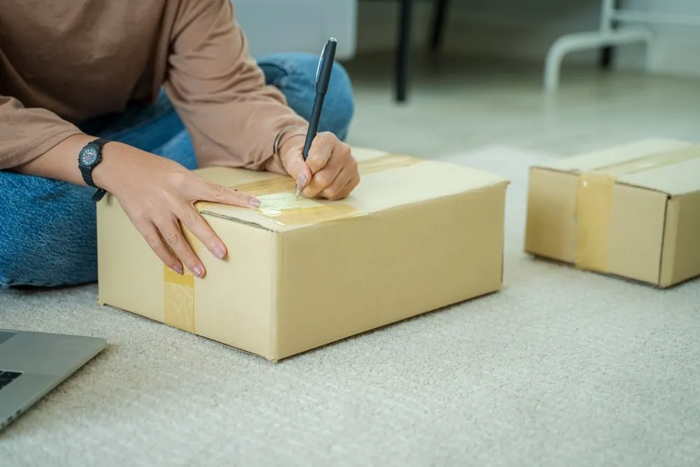 person sat on the floor writing a label on a cardboard box