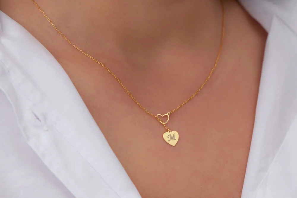 person wearing gold necklace with heart pendant engraved with letter M
