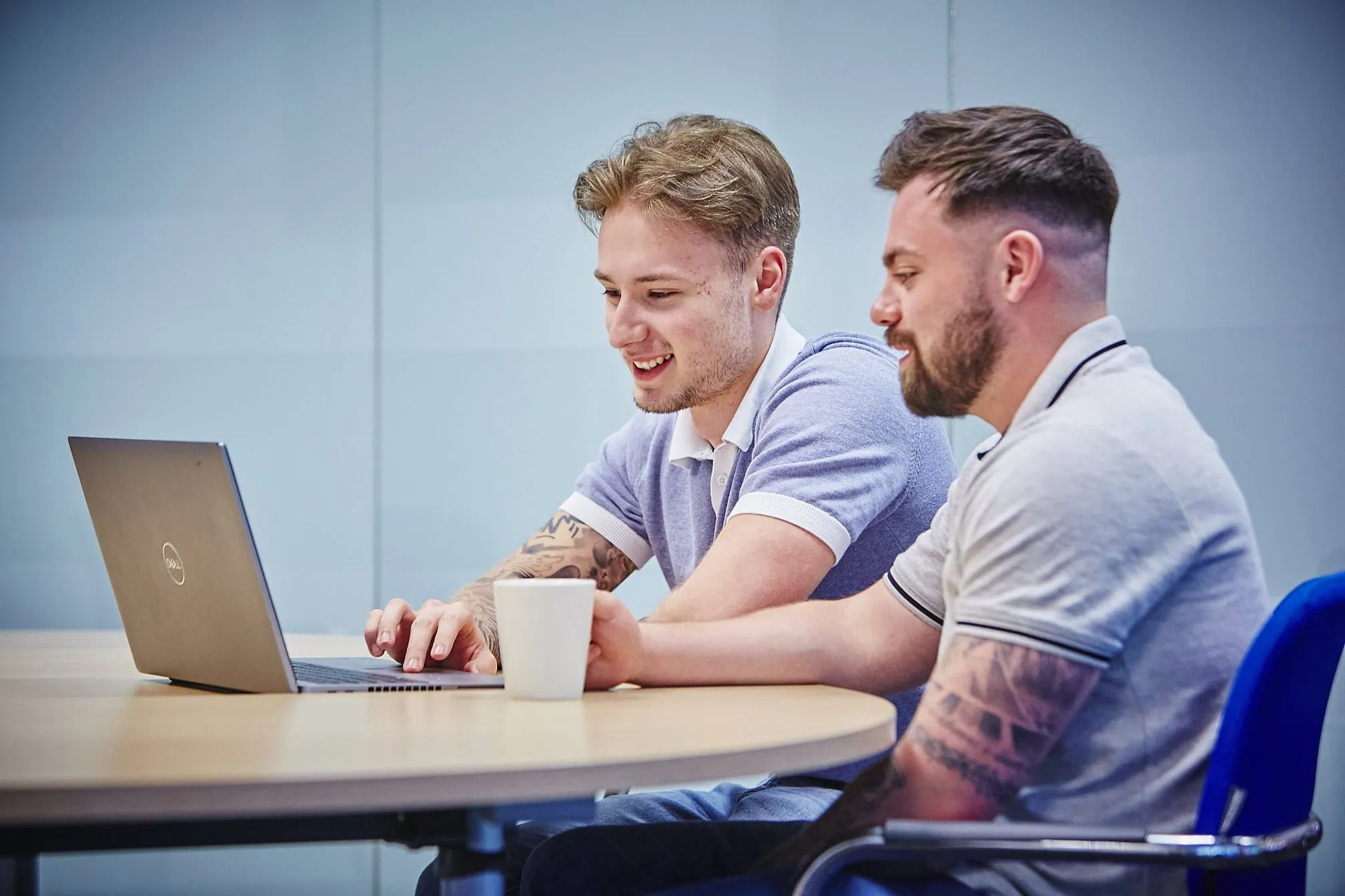 2 men sat at a table smiling at a laptop